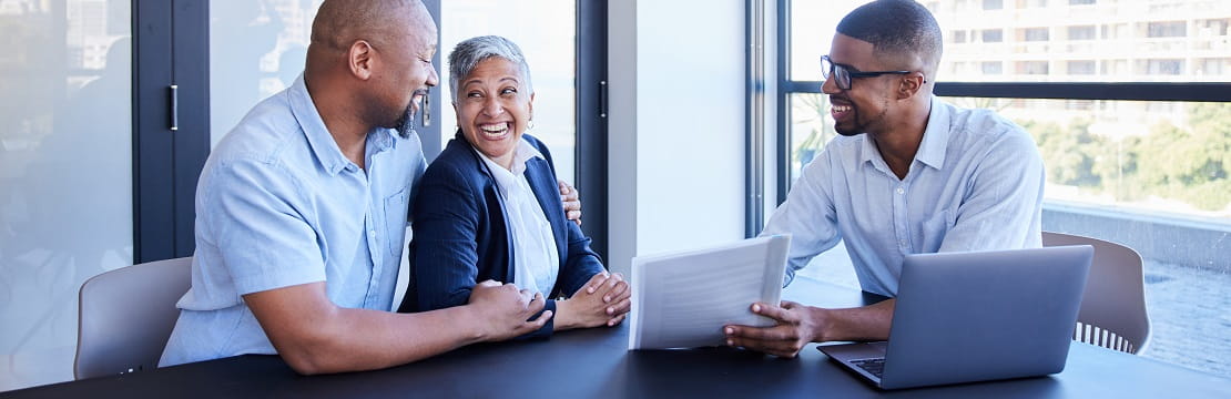 Couple smiling while going over documents with their accountant during a meeting together at table in his office.